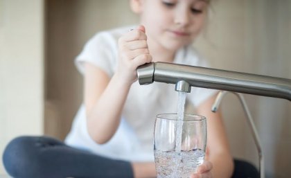 child fills a glass at a water tap